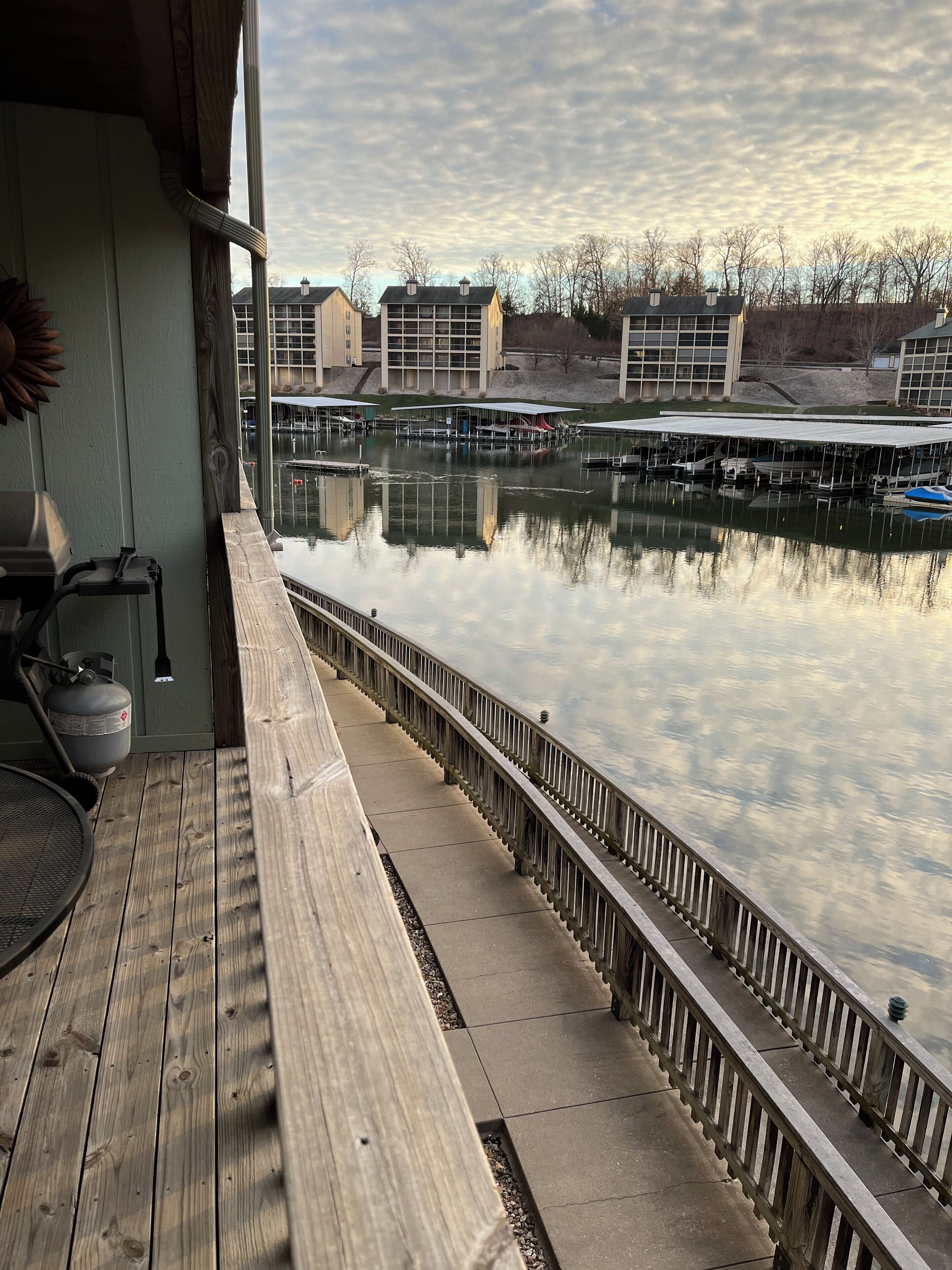En träbrygga med ett räcke som vetter ut mot en stilla vattenyta, med bryggor och byggnader i bakgrunden.