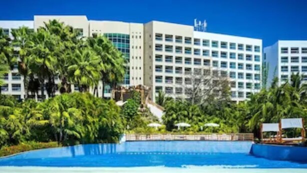 Un hotel con piscina, palmeras y edificios modernos al fondo.