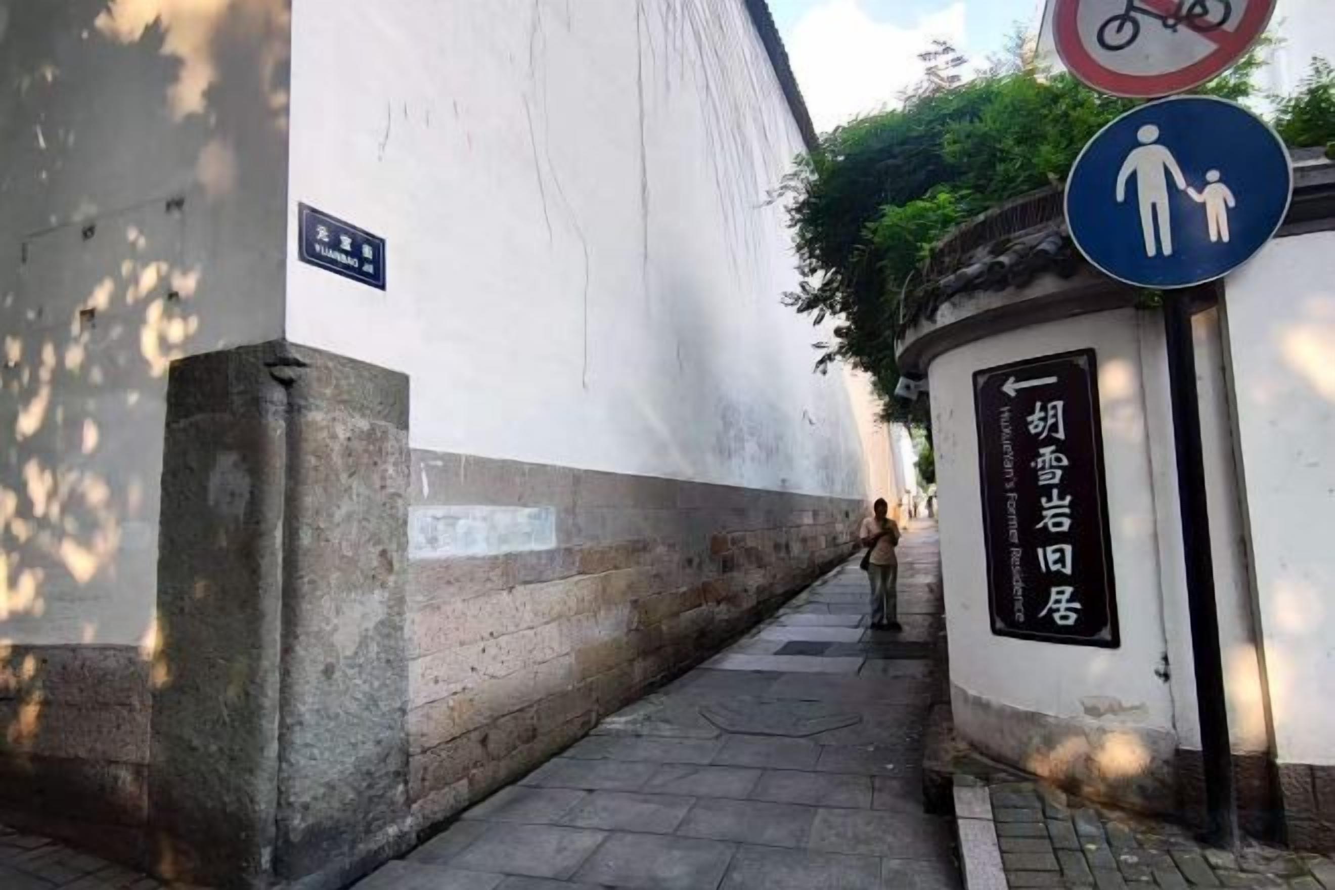Un estrecho callejón con una pared blanca, una base de ladrillo y un letrero con caracteres chinos.