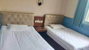 Quarto de hotel com duas camas, uma mesa pequena e uma luminária fixada na parede.