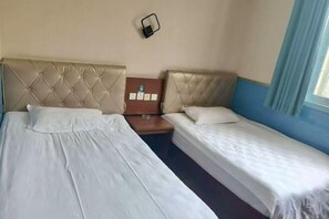 A hotel room with two beds, a small table, and a wall-mounted light fixture.