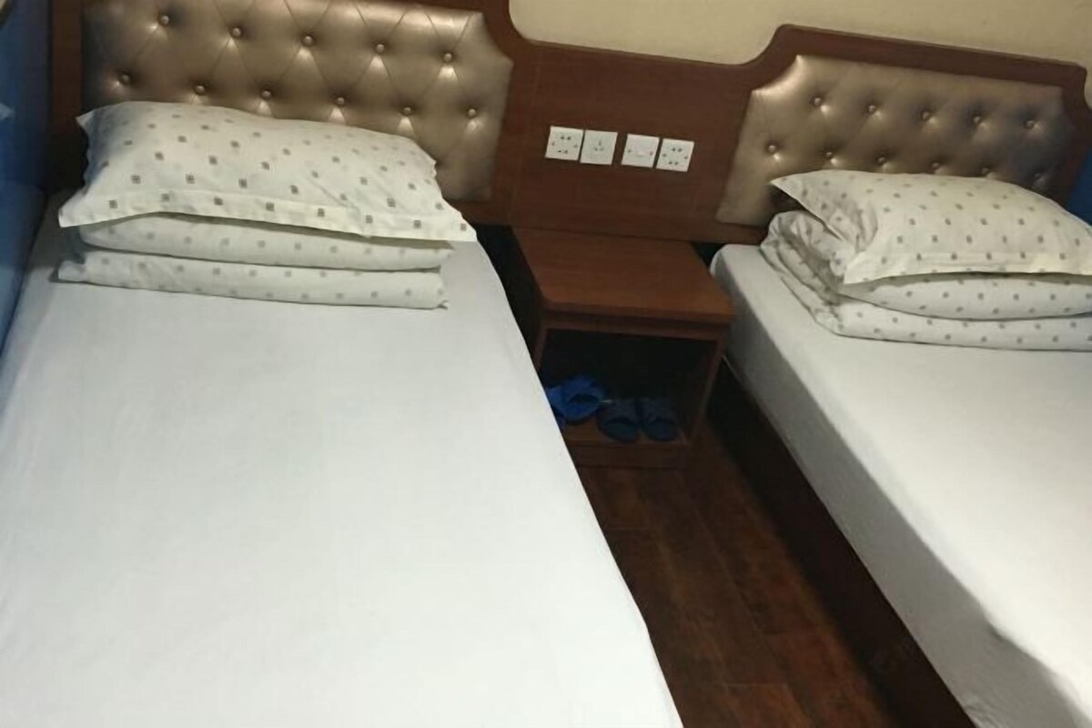 A double bed with a tufted headboard, a wooden nightstand, and a pair of blue slippers on the floor.