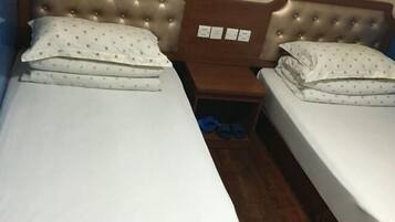 Uma cama de casal com cabeceira estofada, um criado-mudo de madeira e um par de chinelos azuis no chão.