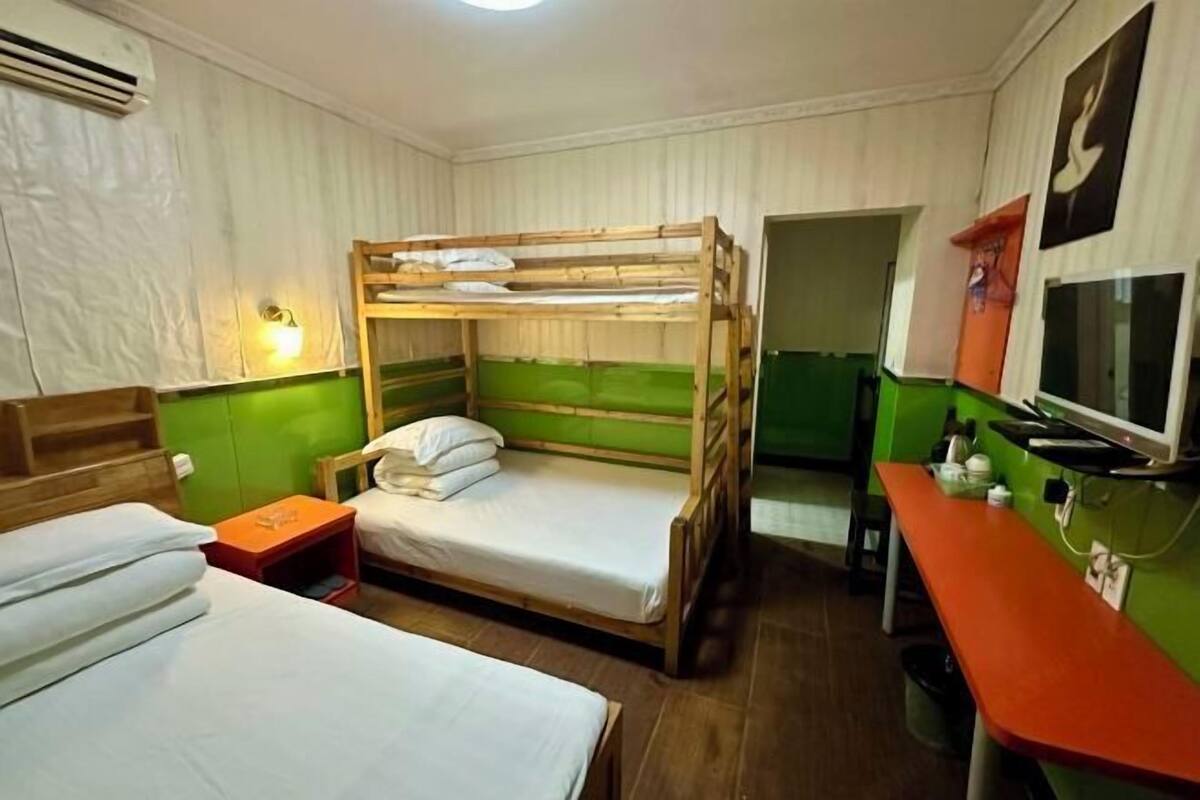 A dormitory room with bunk beds, a desk, a television, and a small table.