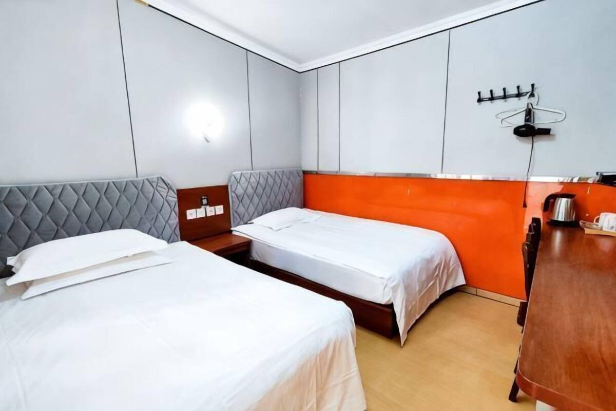 A hotel room with two beds, a wooden desk, a wall-mounted coat rack, and a light fixture.