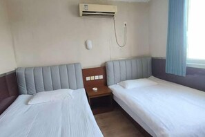 Quarto de hotel com duas camas de solteiro, mesa de cabeceira, ar condicionado e janela com cortina.