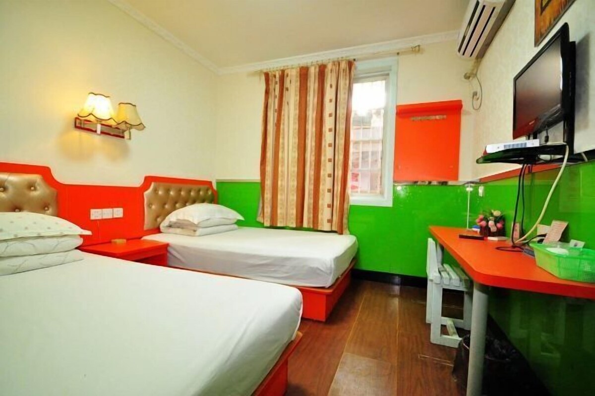 A hotel room with two beds, a desk, a television, and a window with curtains.