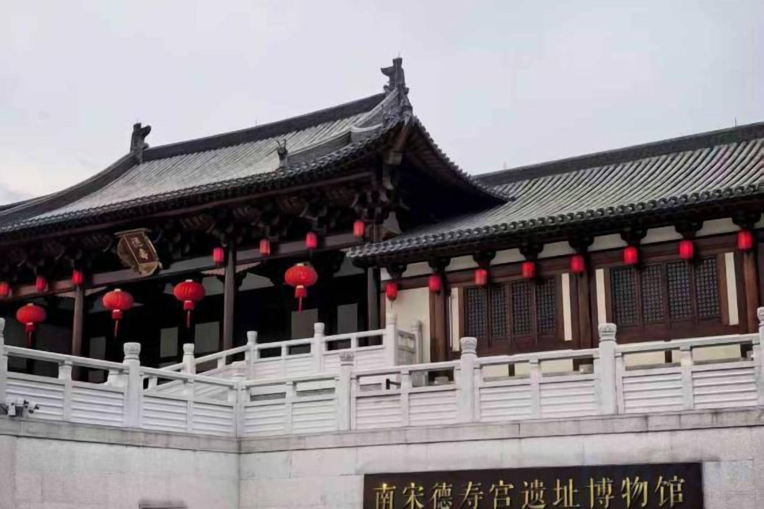 A traditional Chinese building with a tiled roof, red lanterns, and a white railing.