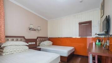 Quarto de hotel com duas camas, uma escrivaninha, televisão e janela com persianas.