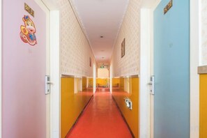 A hotel corridor with a red carpet, doors on both sides, and a sign at the end.