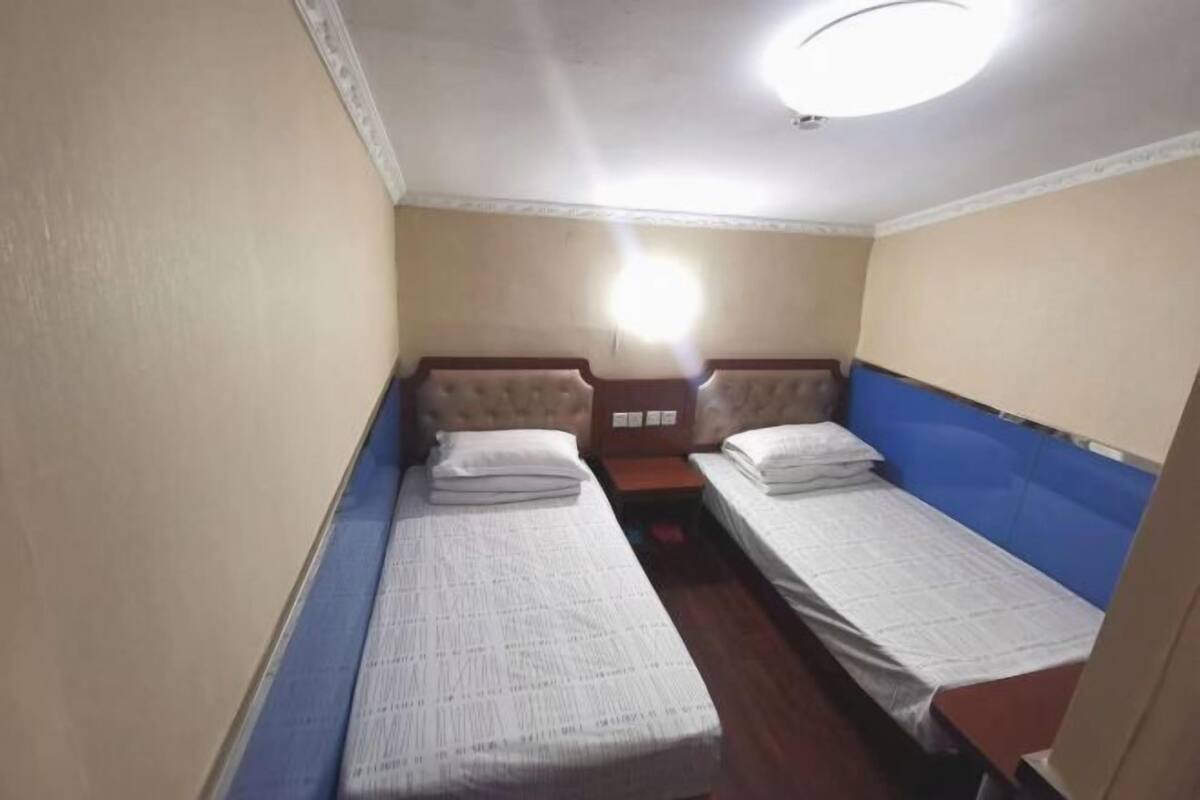 A small, single-room hotel room with two single beds, a wooden floor, and a simple, functional design.