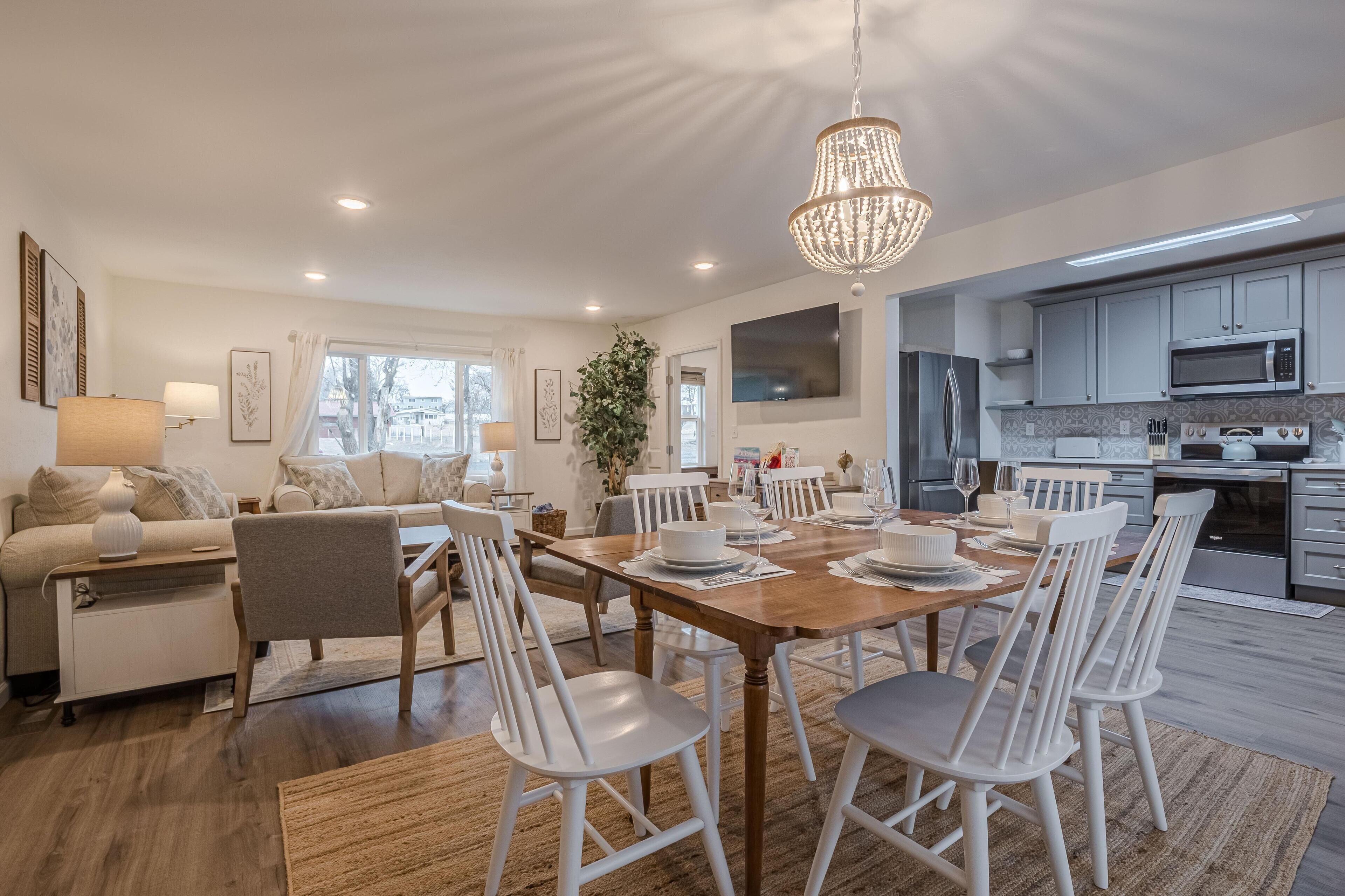 A modern kitchen with white cabinets, a wooden dining table, and a chandelier.