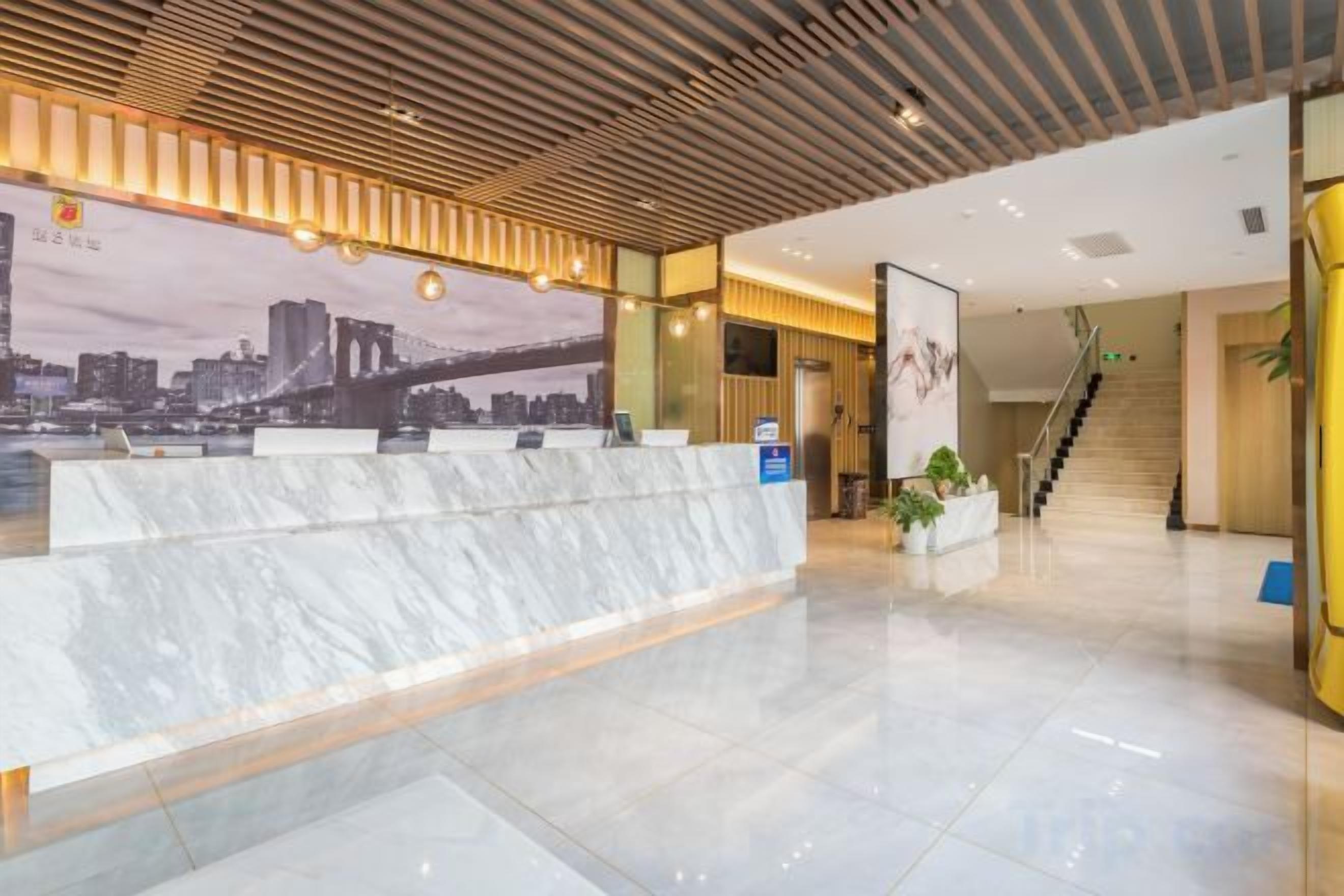 Zona de recepción de hotel con mostrador de mármol, un mural con vista a la ciudad y una escalera que sube a otro piso.