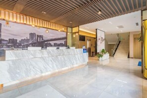 Zona de recepción de hotel con mostrador de mármol, un mural con vista a la ciudad y una escalera que sube a otro piso.