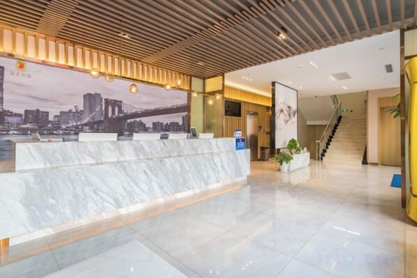 A hotel reception area with a marble counter, a cityscape mural, and a staircase leading to another floor.