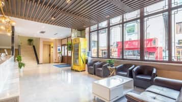 A modern lobby with a reception desk, seating area, and large windows.