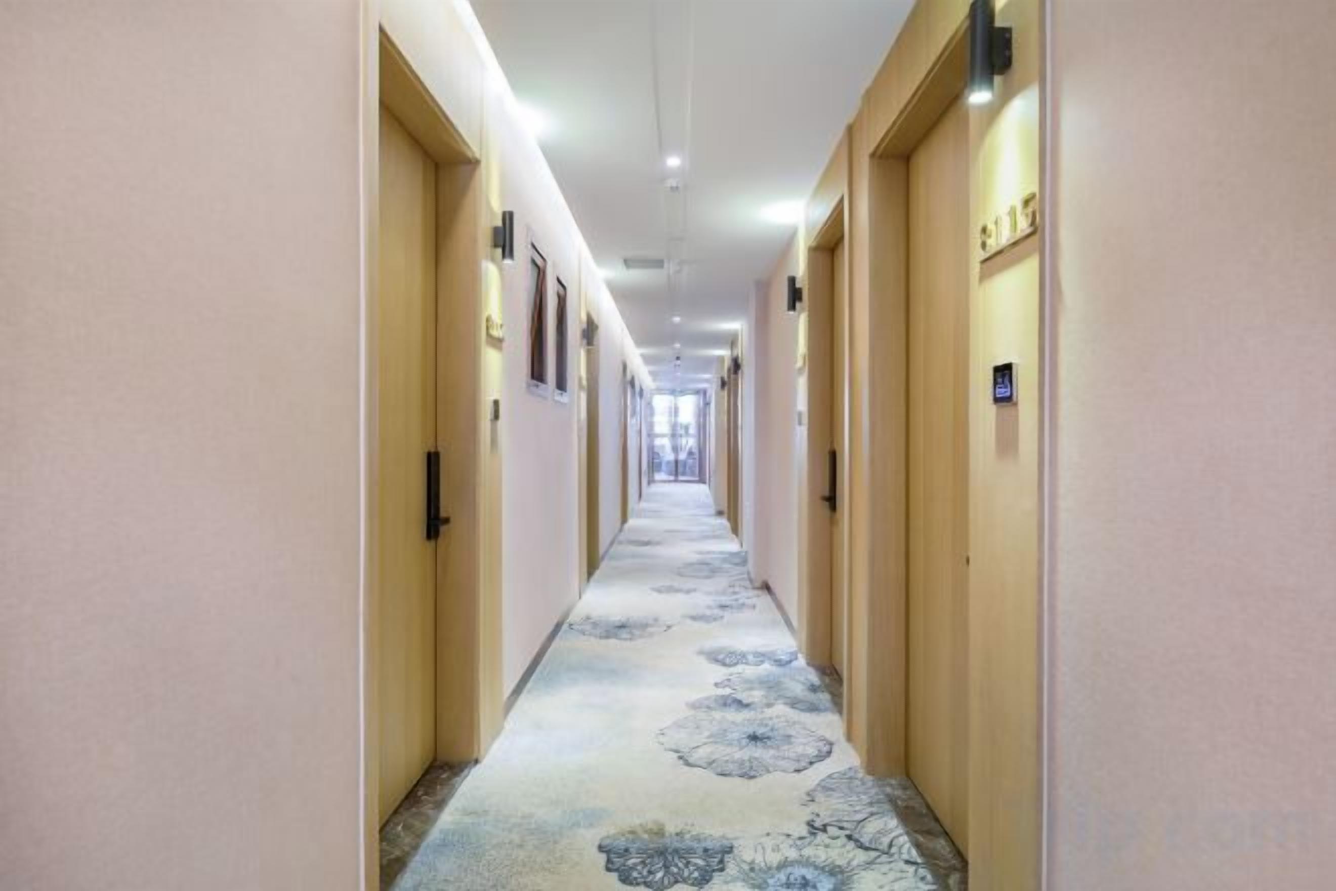 A hotel corridor with doors on both sides, a patterned carpet, and overhead lighting.