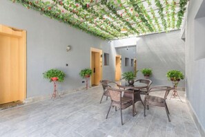 An indoor patio with a dining table and chairs, surrounded by potted plants, and a ceiling with hanging greenery.
