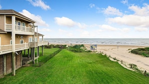 A beachfront hotel with a balcony, a grassy lawn, and a sandy beach.