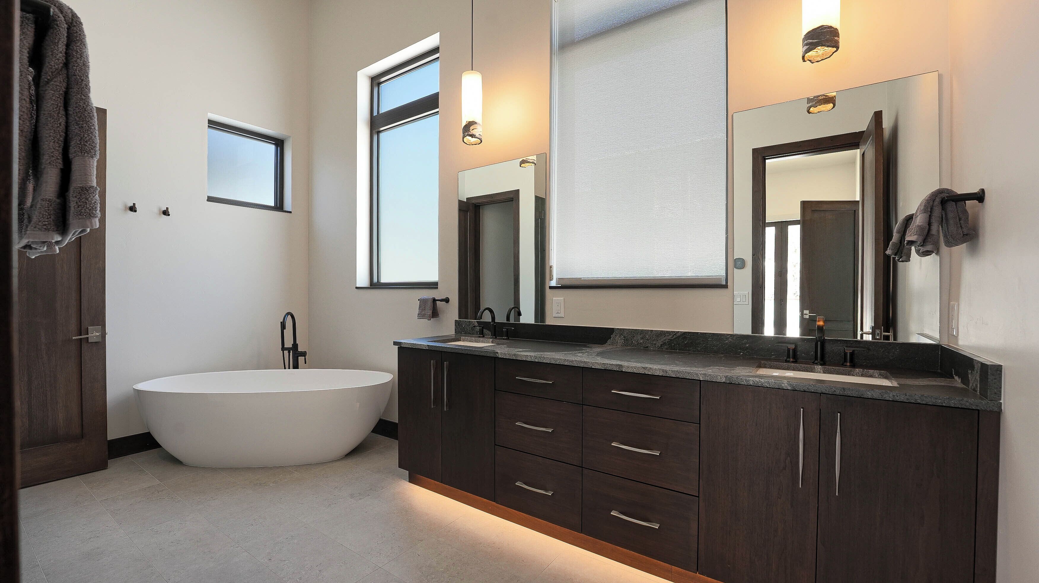 Un baño moderno con una bañera independiente, armarios de madera oscura y un espejo grande.