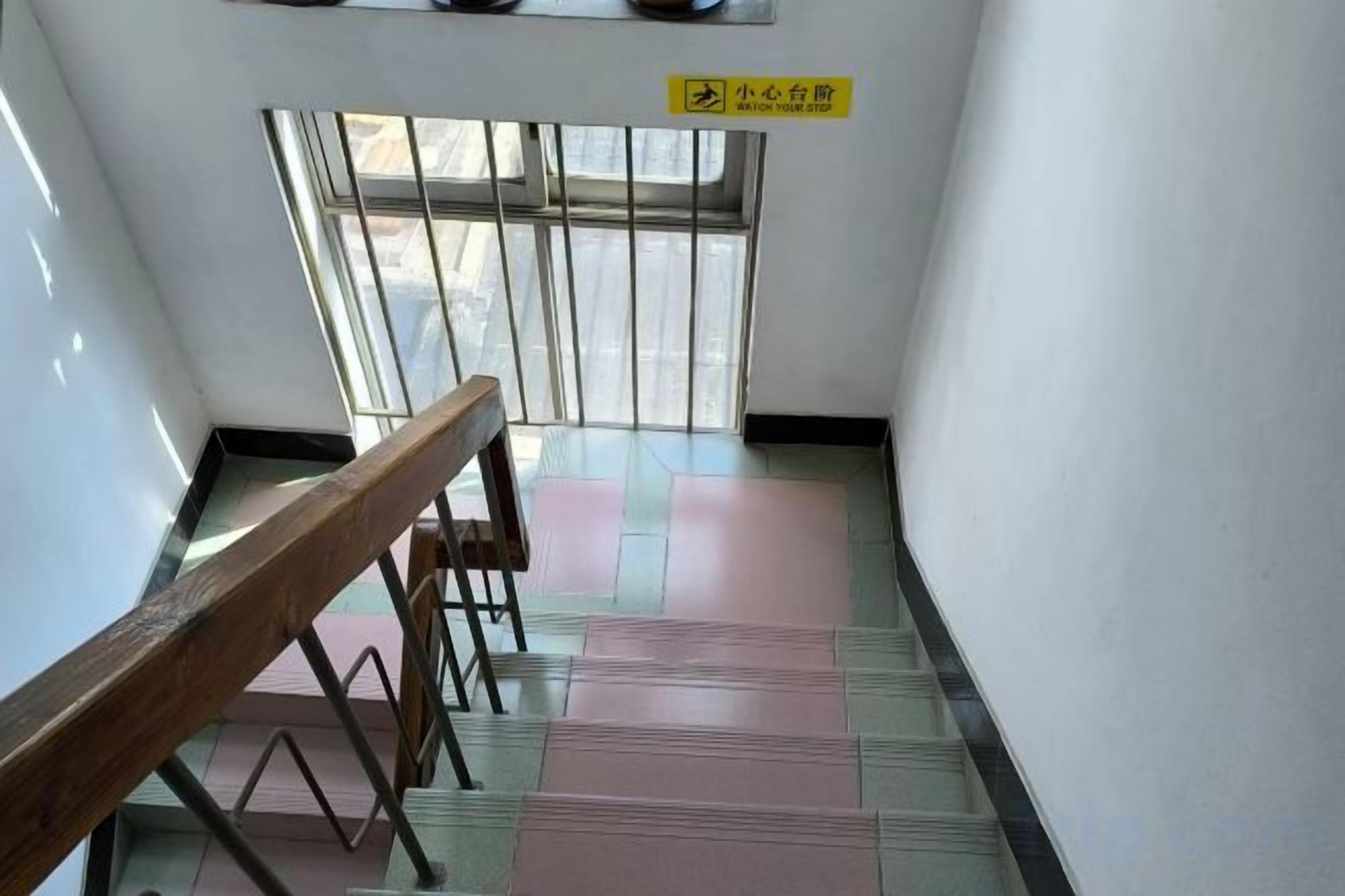 A staircase with a handrail, a window with bars, and a sign indicating a direction.