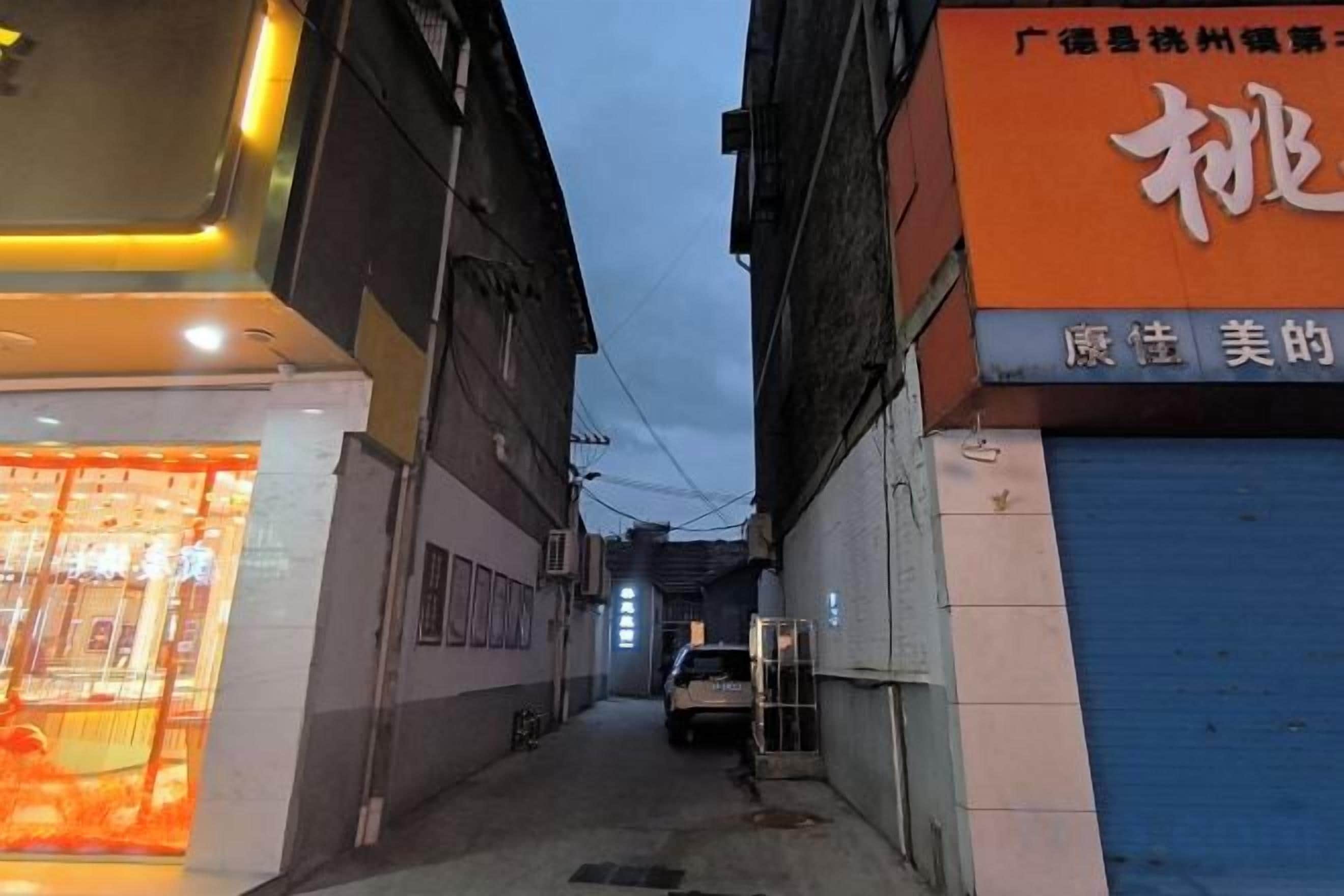 A narrow alleyway with buildings on either side, a parked vehicle, and a closed shop with a visible sign.