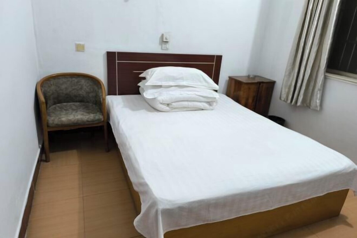 A single bed with a wooden headboard, a chair, a small wooden table, and a window with curtains.