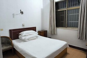 A single bed with white bedding, a wooden headboard, a small bedside table, a chair, and a window with curtains. - Guangde Linyuan Hotel (Guangde)