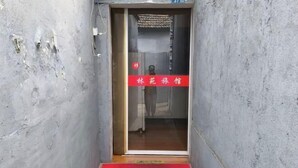 A narrow hallway with a red welcome mat at the entrance, a door with a red sign, and a number 37 on the wall.