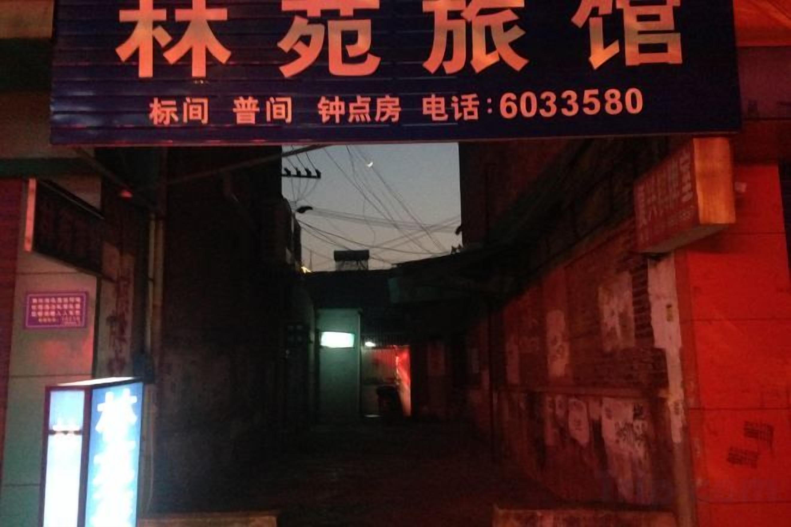 A narrow alleyway with a sign for a hotel. The sign includes the hotel's name and contact number.