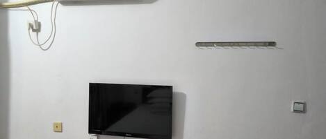 A room with a mounted TV, a white air conditioner, and a power strip on the wall.