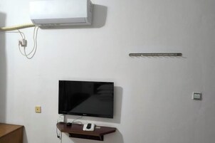 Quarto com televisão montada na parede, ar condicionado branco e régua de tomadas.