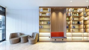 Un espace de lecture moderne avec des fauteuils en osier, une bibliothèque et un banc rouge.