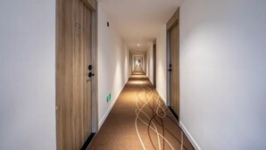 Un long couloir étroit, typique d’un hôtel, avec des portes en bois de chaque côté et un sol recouvert de moquette.