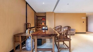 Un coin repas avec une table et des chaises en bois, une petite table d’appoint avec un plateau, et une bibliothèque en arrière-plan.