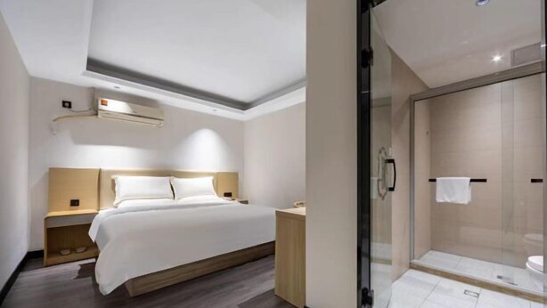 Une chambre d’hôtel moderne équipée d’un lit, d’une table de chevet et d’une cabine de douche en verre.