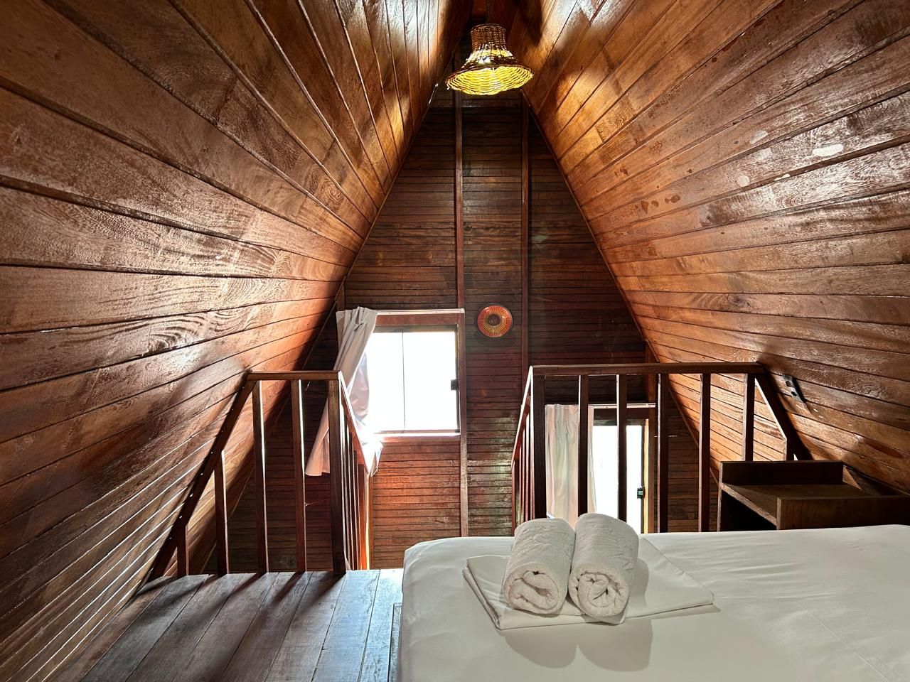 A wooden attic bedroom with a bed, a window, and a staircase.