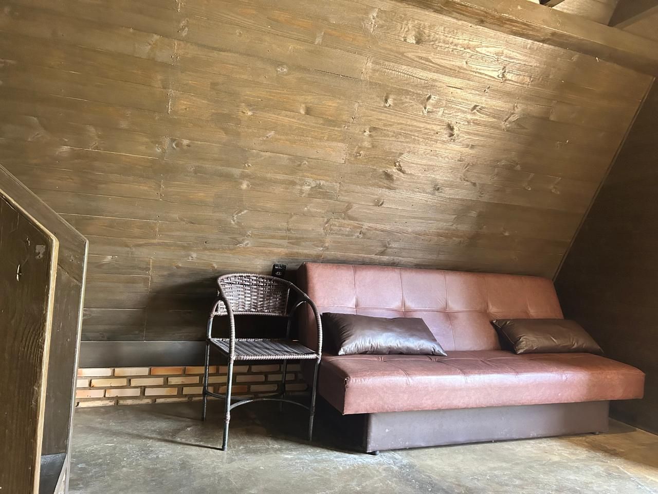 Una habitación con un sofá de cuero marrón, un sillón de mimbre y una pared de ladrillo.