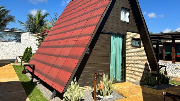 Una casa moderna con techo rojo inclinado, fachada de ladrillo y una ventana pequeña con cortina.