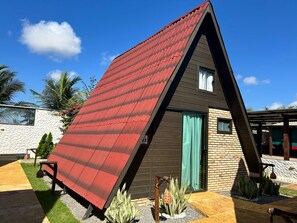 Une maison moderne avec un toit rouge à pente, une façade en briques et une petite fenêtre ornée d’un rideau.