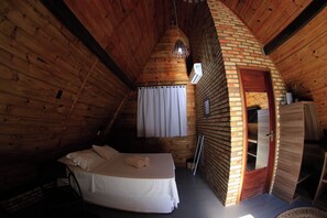 A cozy wooden cabin room with a bed, a hanging light fixture, and a small window with curtains. - Pousada Bellíssima Itália (Luis Correia)