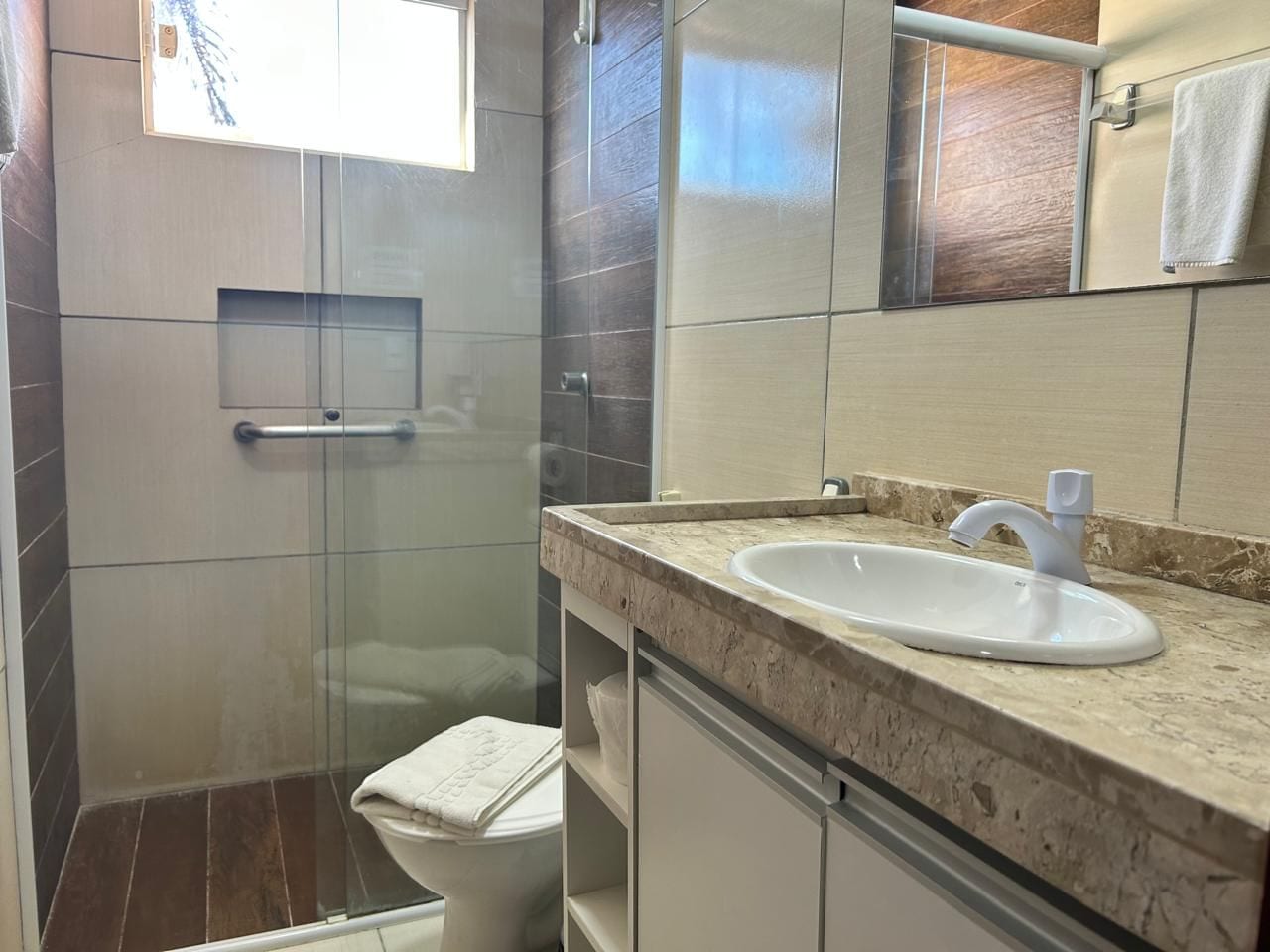 A bathroom with a glass shower enclosure, a toilet, and a sink with a marble countertop.