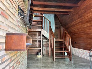 Un escalier en bois menant à un niveau supérieur, une étagère en métal et un mur en briques.