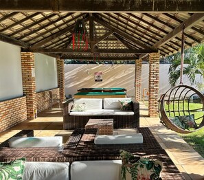 Un patio exterior con una zona de estar cubierta, una silla colgante y una pared de ladrillo.