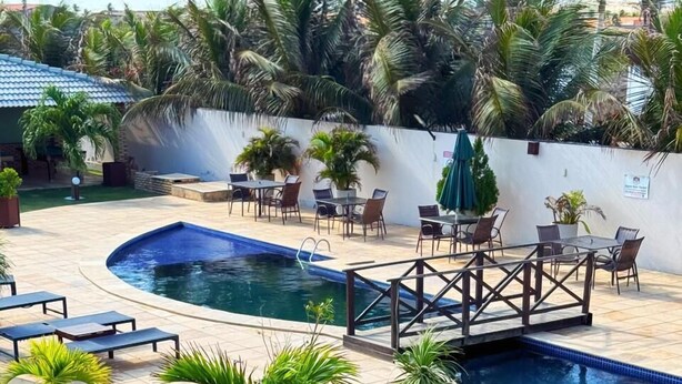 A swimming pool with lounge chairs and tables, surrounded by palm trees and a white wall. - Grupo Al Mare e Bellissima (Luis Correia)