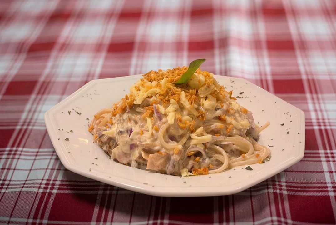 Plat de pasta amb una salsa cremosa, decorat amb cimbros fregits i una fulla verda, damunt d'un plat blanc.