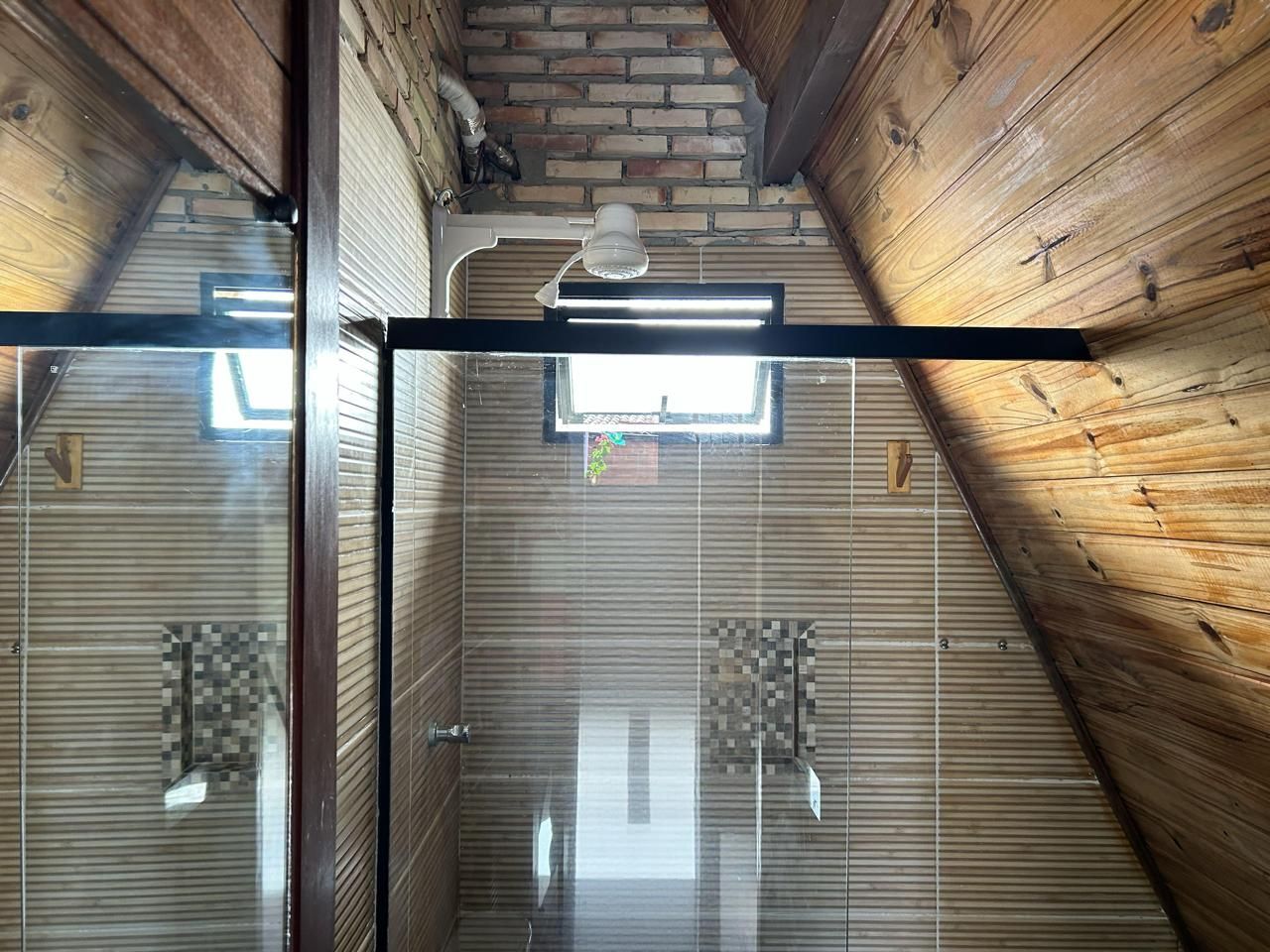Ducha con puerta de vidrio, techo de madera y tragaluz.