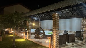 An outdoor patio area with a covered seating area, brick pillars, and hanging chairs. - Grupo Al Mare e Bellissima (Luis Correia)