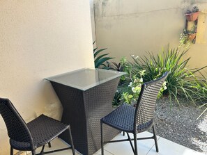 Ein Tisch mit Glasplatte und zwei Korbstühle, vor einer Wand mit Topfpflanzen platziert.