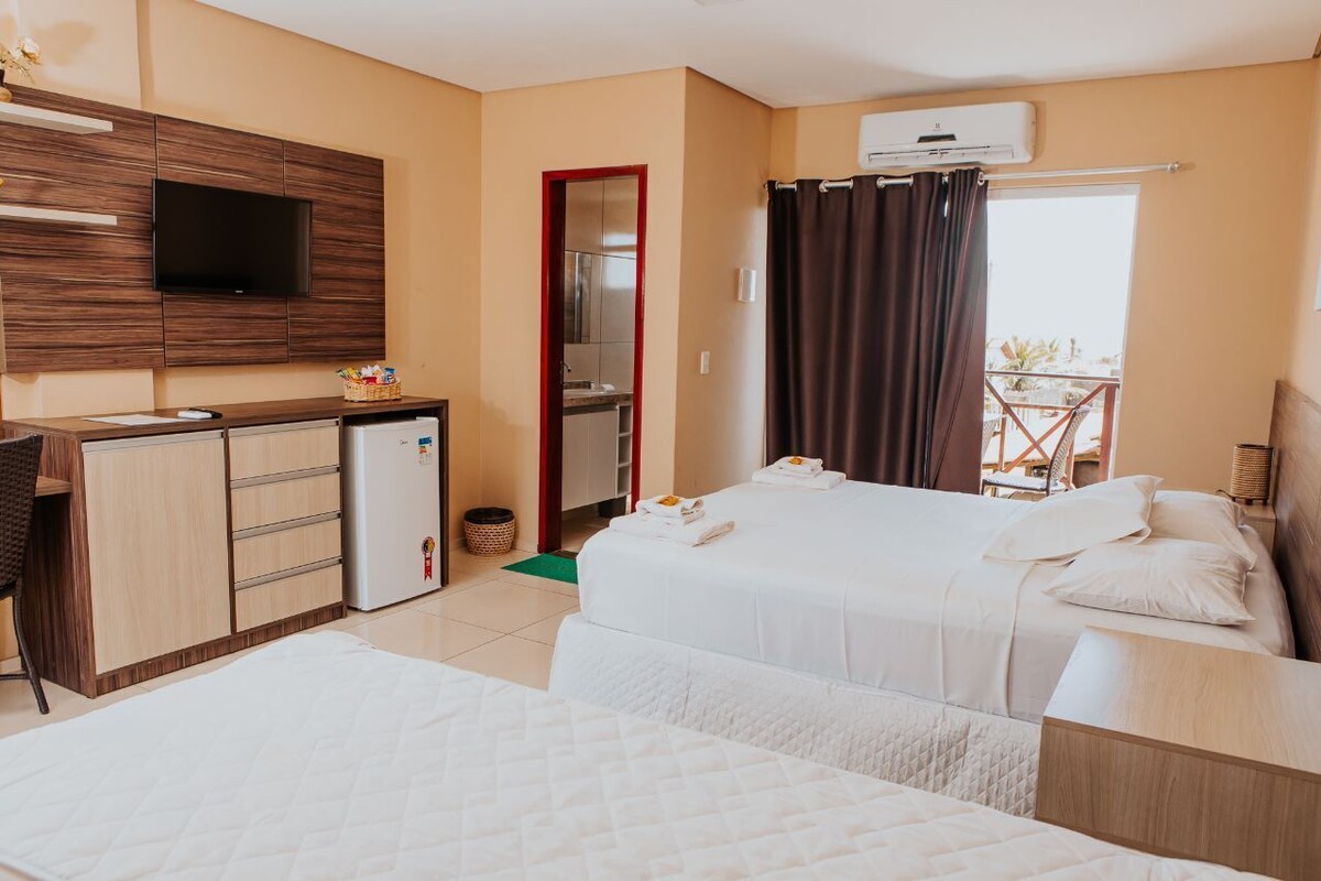 A hotel room with two beds, a TV, a kitchenette, and a balcony.